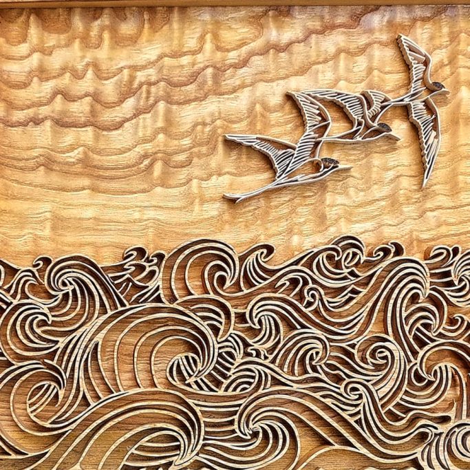 Wood carving depicting waves and two birds in flight against a textured background.