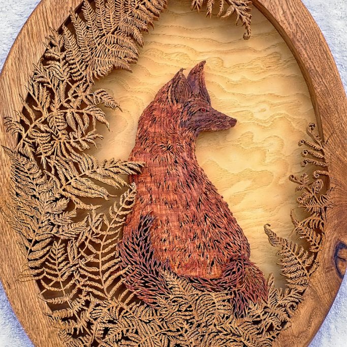 Wooden carving of a fox surrounded by intricately designed ferns.