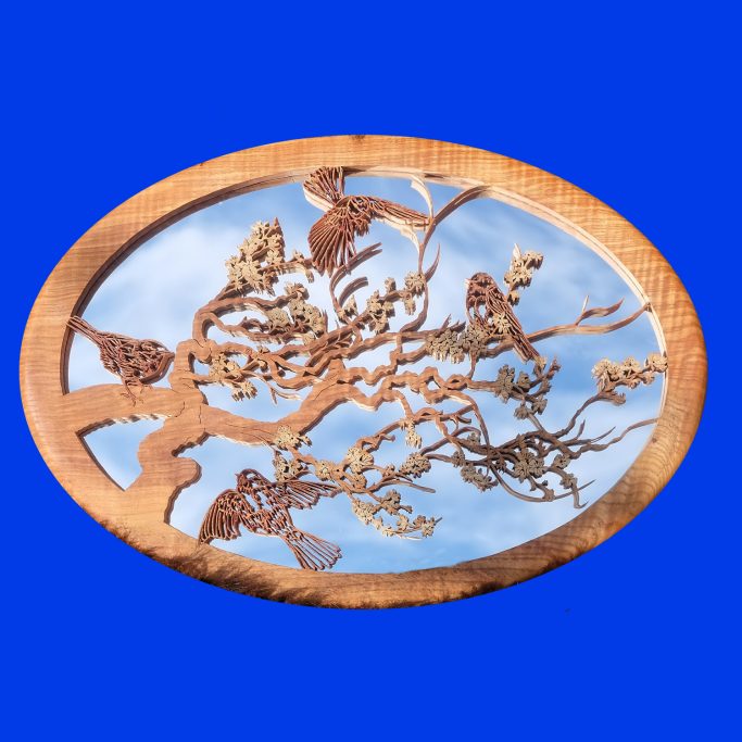 Intricate filigree wood scene of birds amongst branches over a mirror reflecting blue sky and clouds