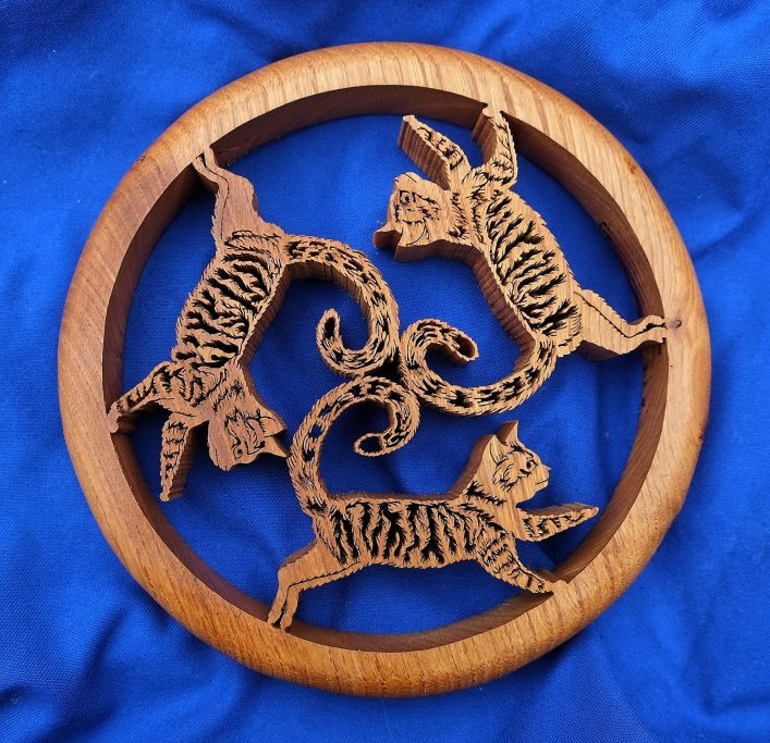 Wooden decoration featuring three leaping cats in a circular design.