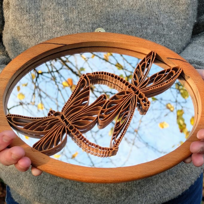A wooden mirror with intricately carved dragonflies and autumn leaves reflected in it.