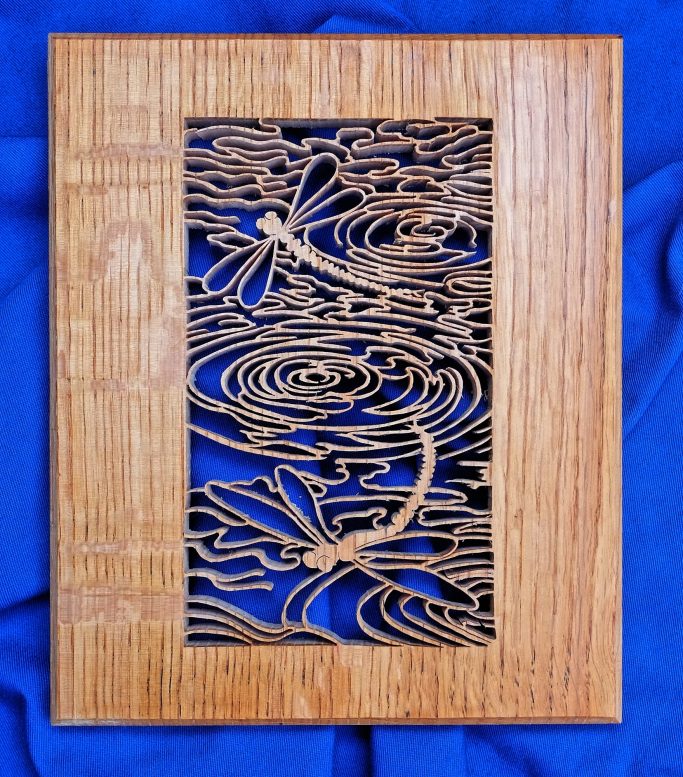 Pierced wood art depicting dragonflies over water ripples
