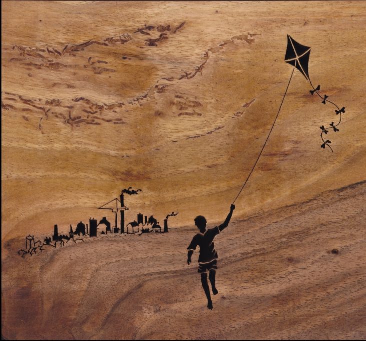 Child flying a kite with a city skyline in the background, depicted cut into wood.