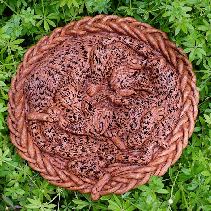 Intricate wooden carving of kittens in  a circular braided frame.