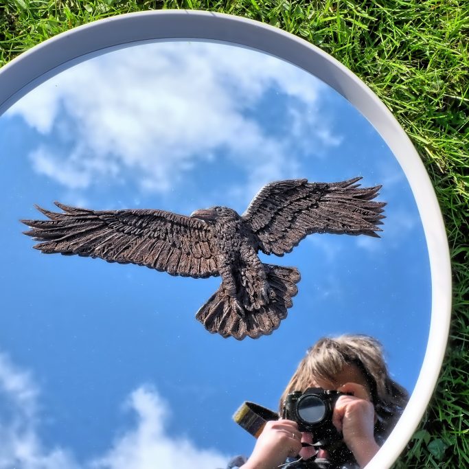 A photographer capturing a carved ravens reflection in a circular mirror outdoors.