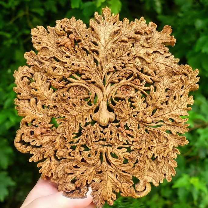 Intricately carved wooden face surrounded by leafy foliage.