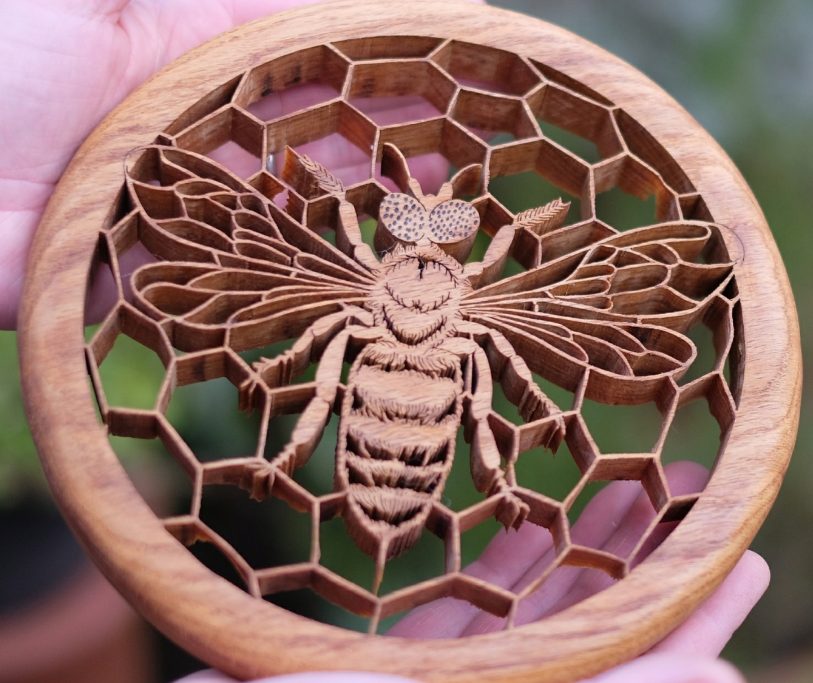 Wooden decorative piece featuring a bee surrounded by a honeycomb pattern.