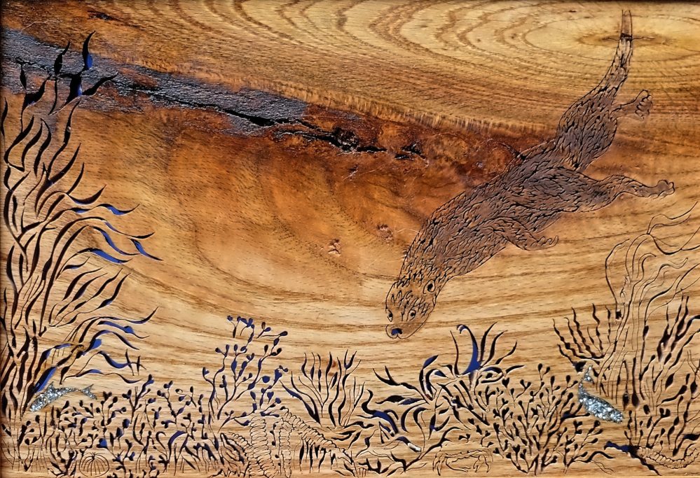 Wooden art featuring an intricate design of an otter and and aquatic plants.