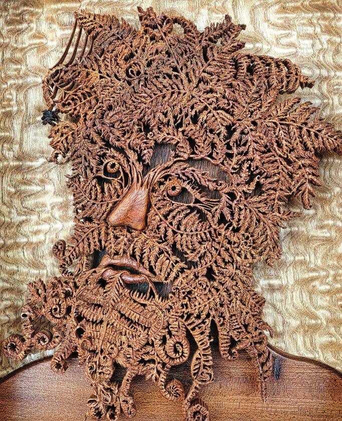 Wooden sculpture of a face with intricate, swirling patterns for hair and beard.