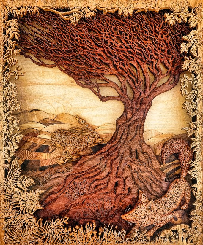 Intricate hand carved landscape featuring a fox and hare chasing around a tree with fields in the background